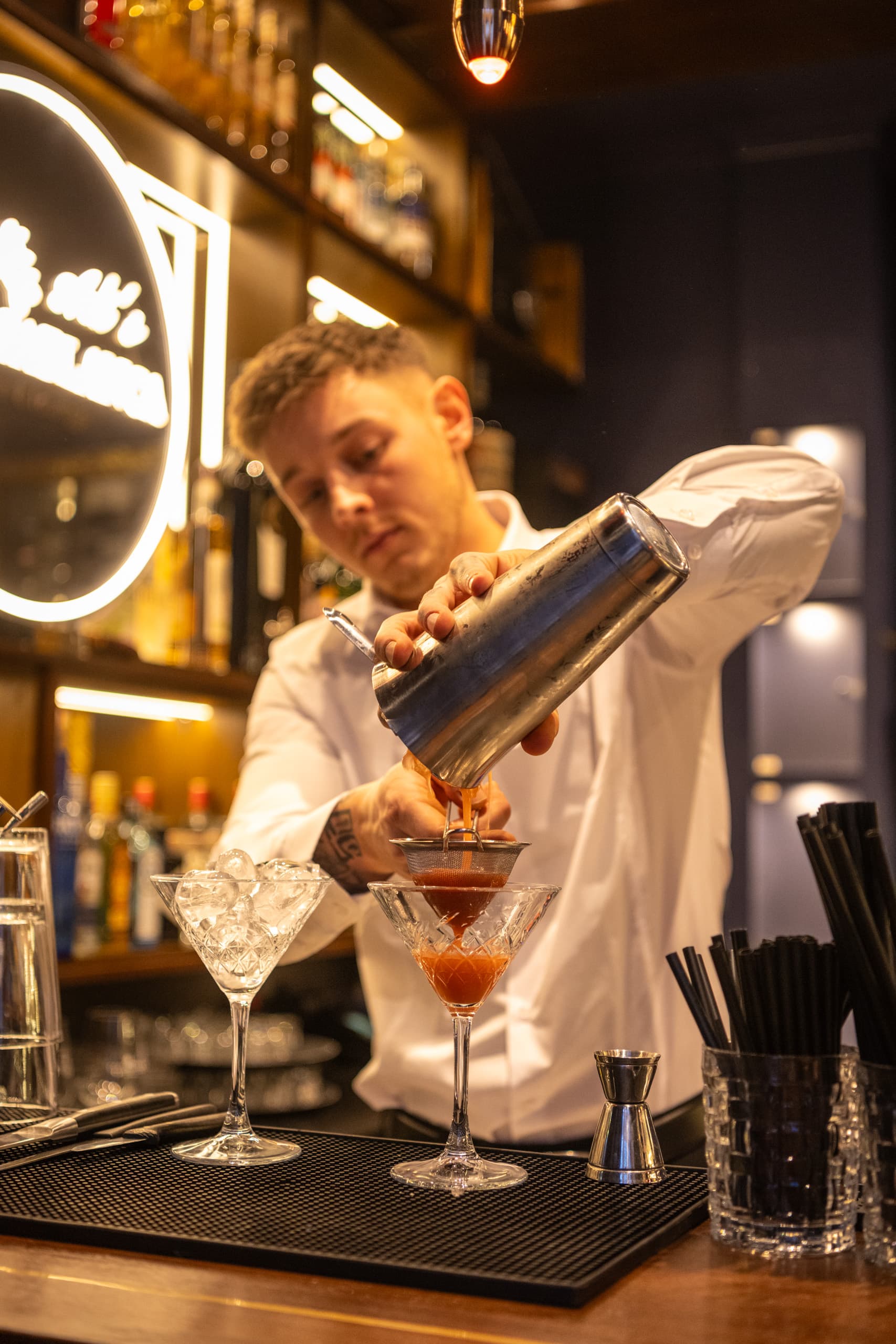 Ein Barkeeper gießt einen Cocktail durch ein Sieb ins Glas