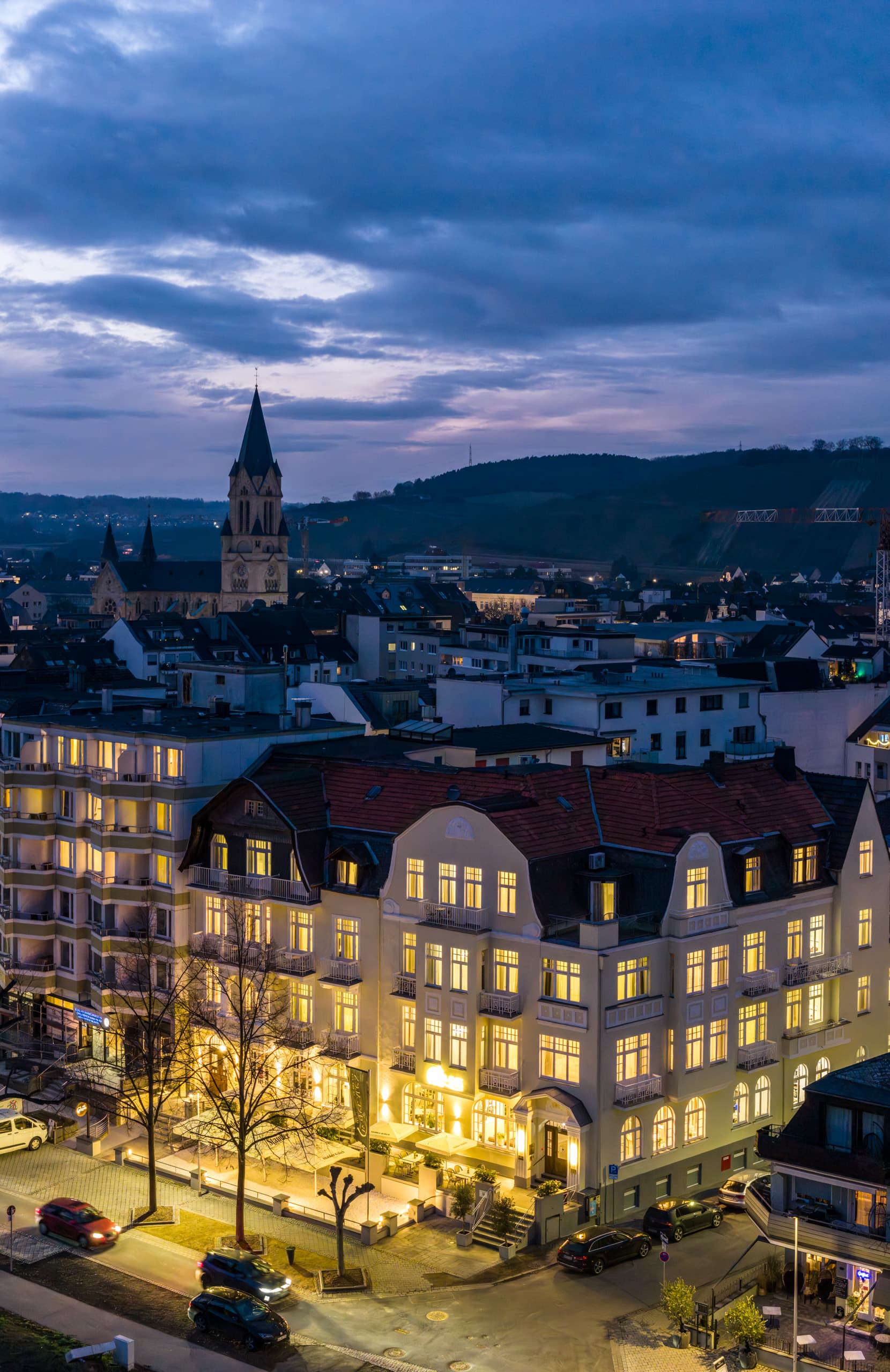 Blick auf das beleuchtete Hotel und Bad Neuenahr mit Kirche und Hügeln im Hintergrund