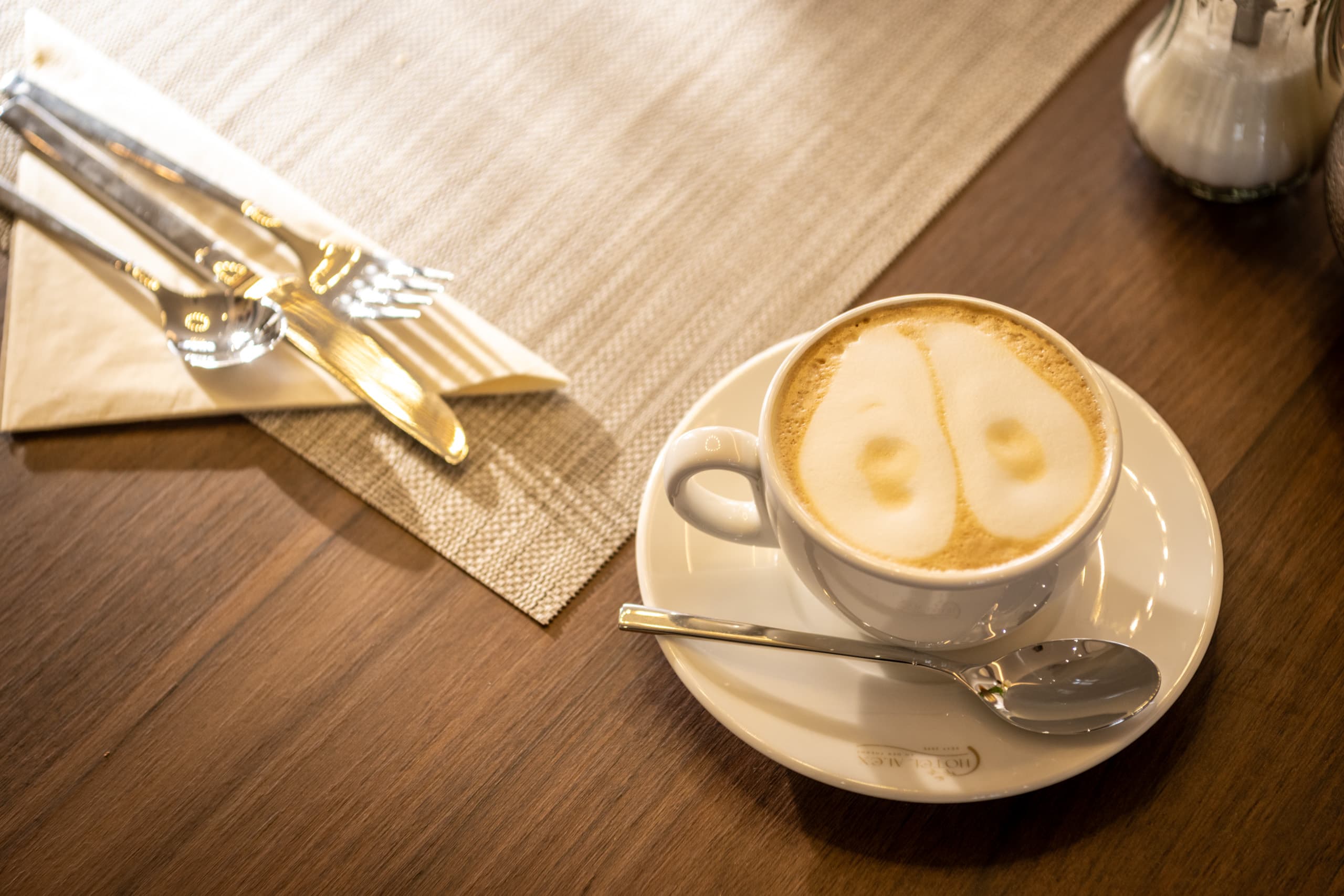 Tasse Kaffee mit Milchschaum am gedeckten Frühstückstisch