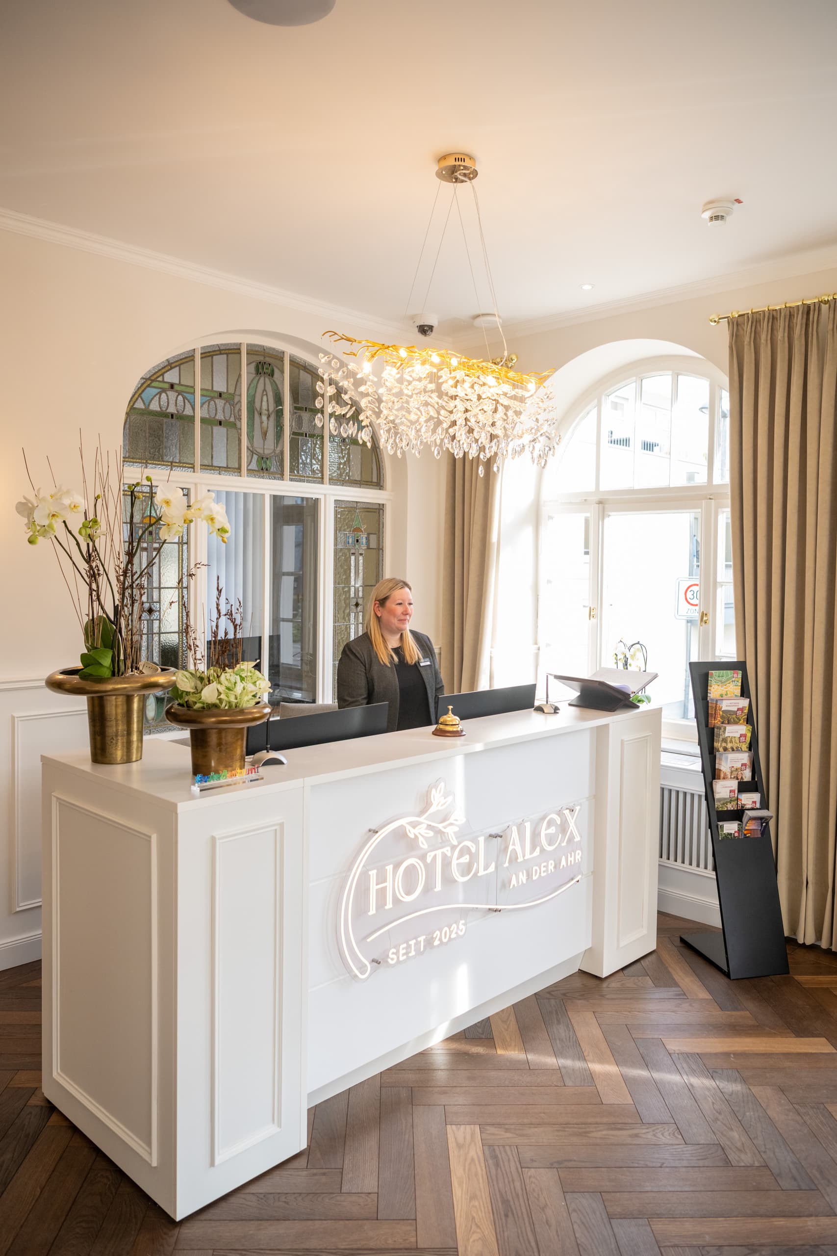 Empfang mit weißer Hotel-Alex-Rezeption, Buntglasfenster und Kronleuchter